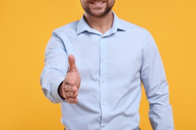 Photo of Man welcoming and offering handshake on yellow background, closeup