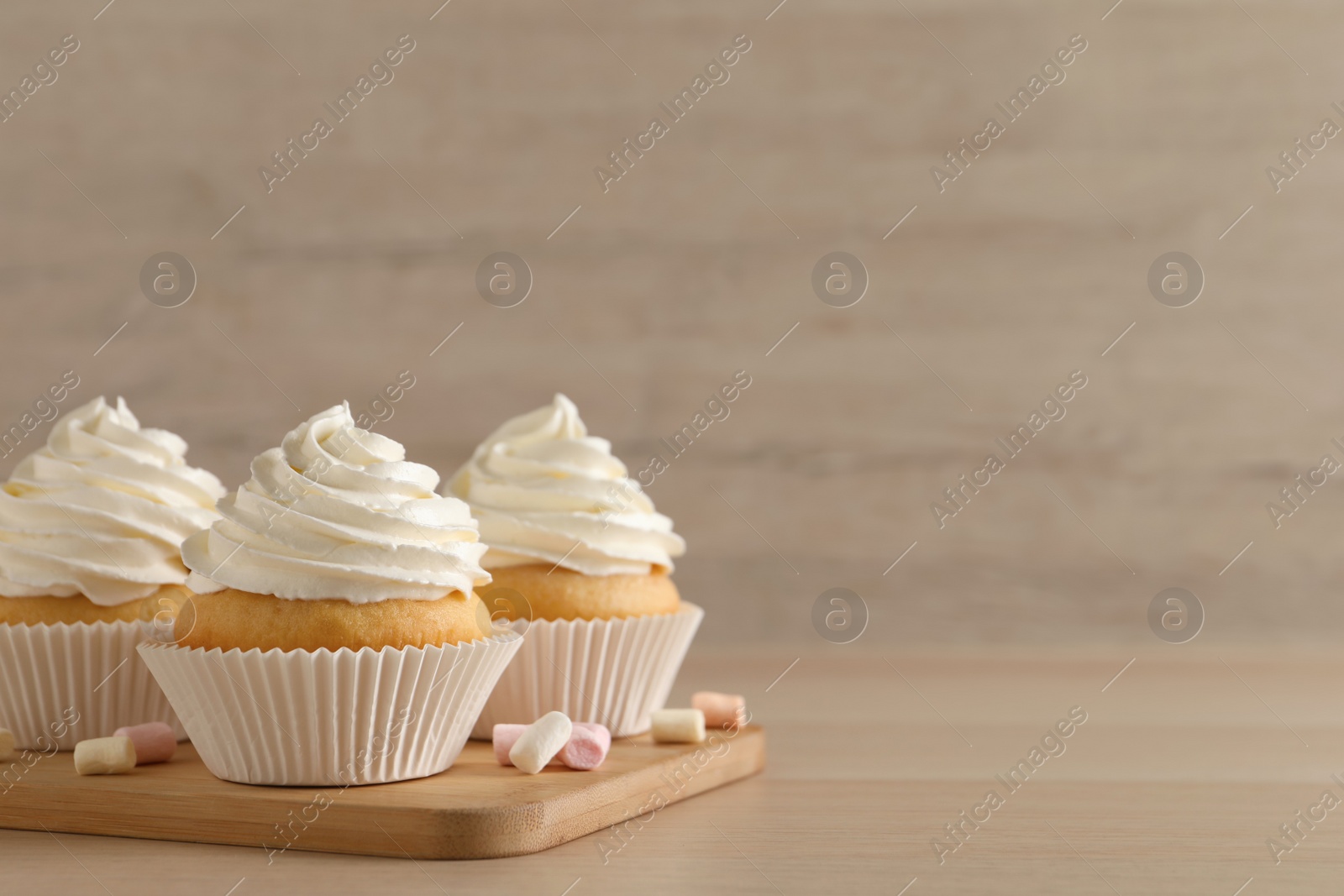 Photo of Delicious cupcakes with cream and marshmallows on wooden table. Space for text