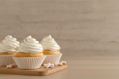 Photo of Delicious cupcakes with cream and marshmallows on wooden table. Space for text