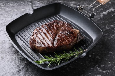 Grill pan with delicious fried beef meat and rosemary on grey textured table