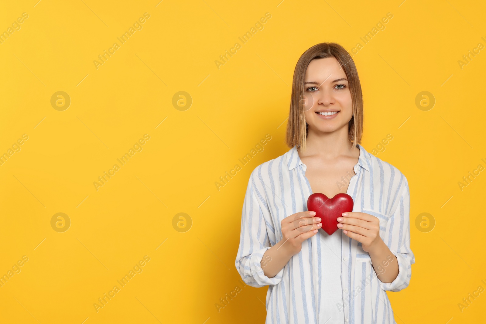 Photo of Young woman holding red heart on yellow background, space for text. Volunteer concept