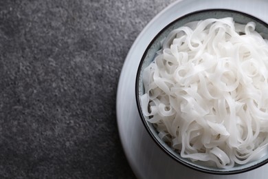 Photo of Bowl of tasty cooked rice noodles on grey table, top view. Space for text