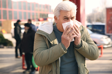 Photo of Sick senior man with tissue on city street. Influenza virus