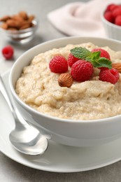Photo of Tasty oatmeal porridge with raspberries and almond nuts served on table, closeup