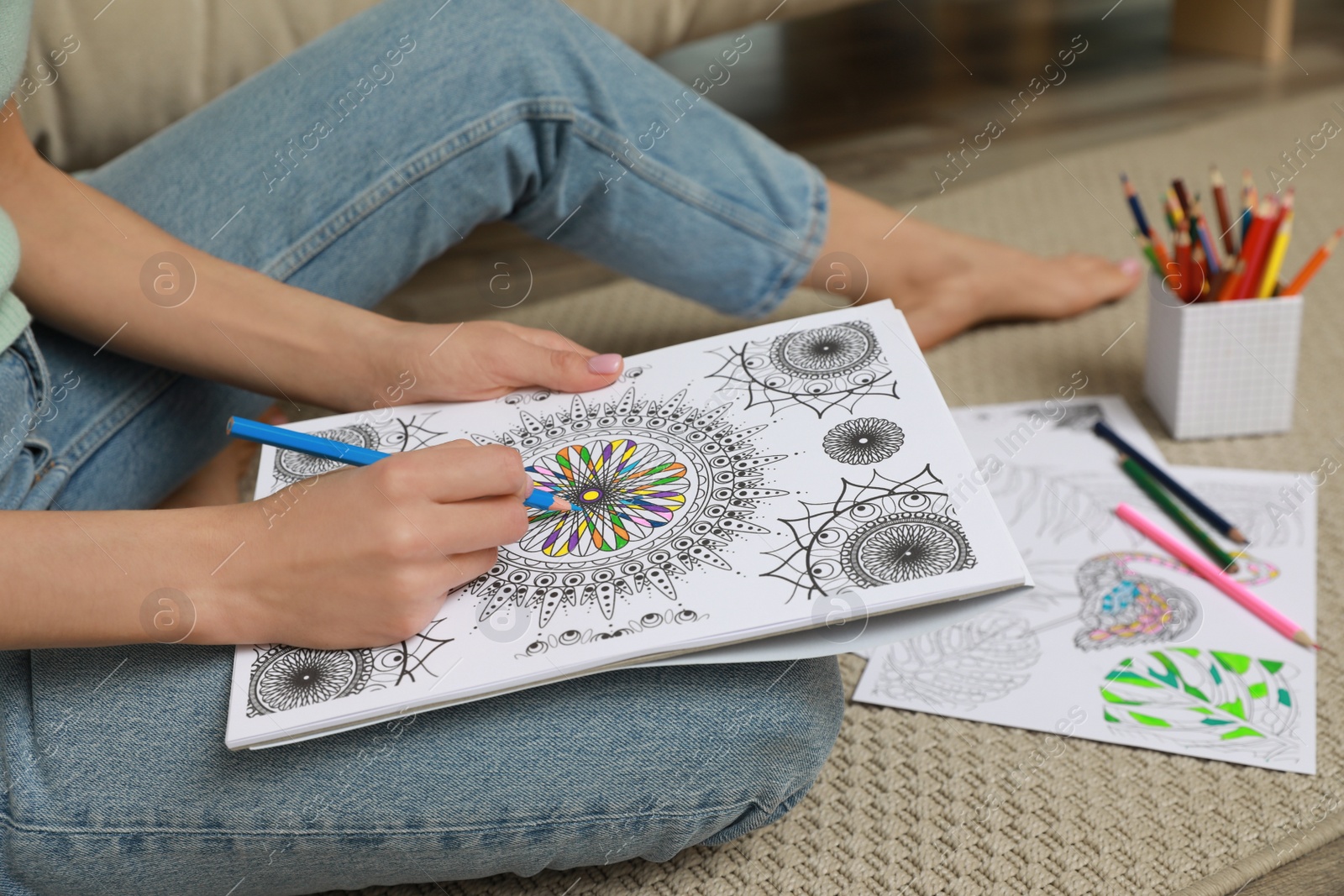 Photo of Young woman coloring antistress page on floor, closeup