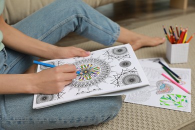 Photo of Young woman coloring antistress page on floor, closeup