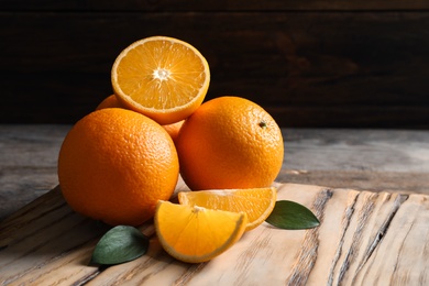 Photo of Fresh oranges with leaves on wooden table, space for text