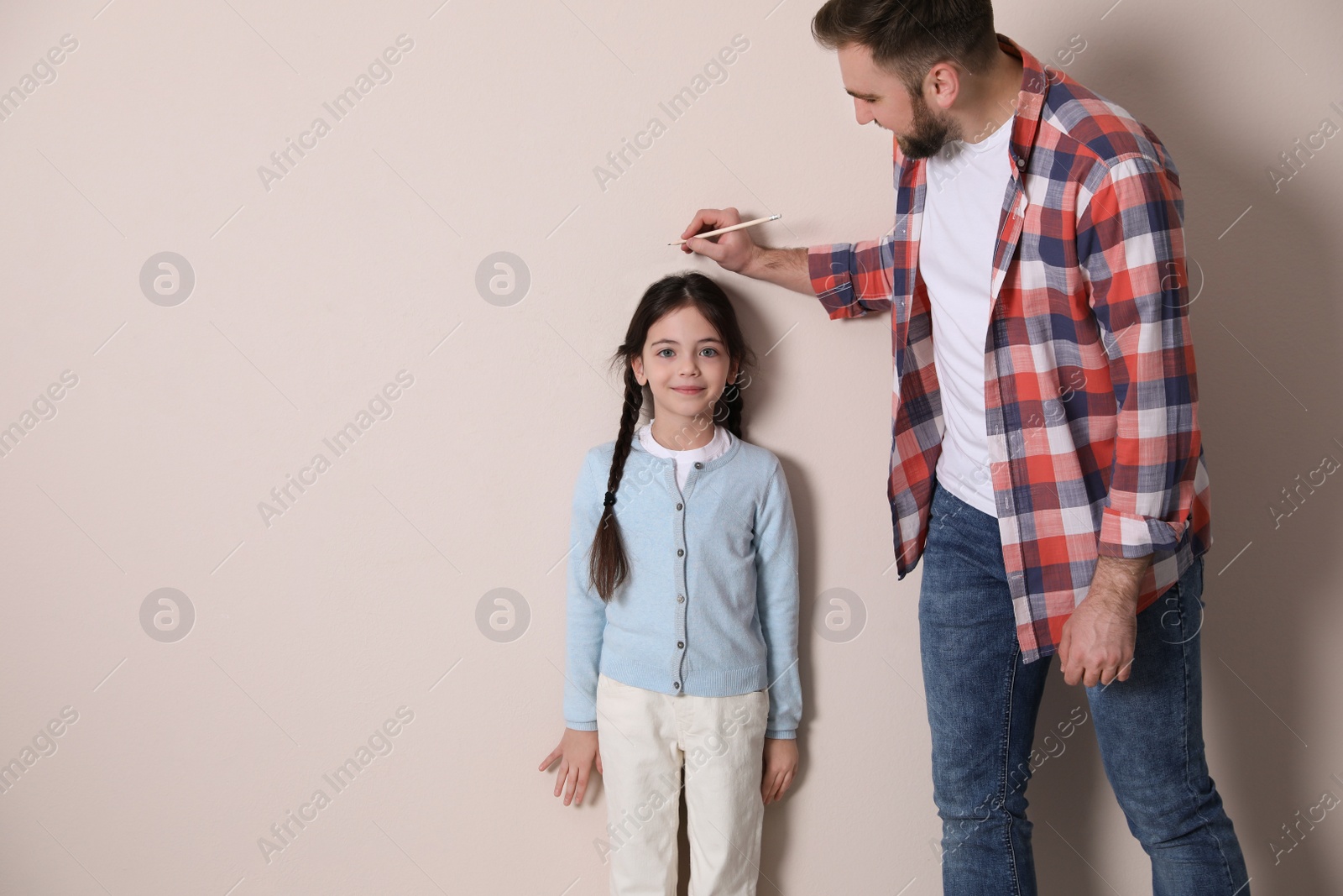 Photo of Father measuring daughter's height near beige wall, space for text