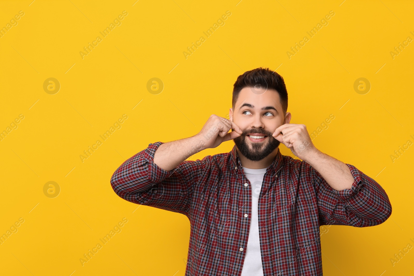 Photo of Happy young man touching mustache on yellow background. Space for text