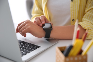 Woman with laptop using smartwatch at white table, closeup