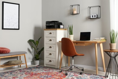 Photo of Stylish room interior with chest of drawers, modern printer and laptop