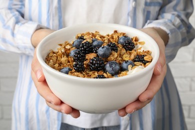Photo of Woman holding bowl of oatmeal porridge with berries, closeup