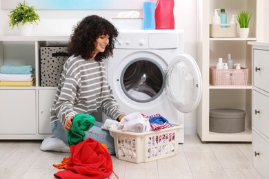 Photo of Happy woman with laundry near washing machine indoors