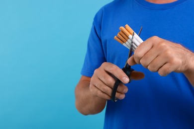 Stop smoking concept. Man cutting cigarettes on light blue background, closeup. Space for text