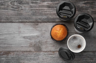 Photo of Coffee to go. Paper cups of tasty drink and muffin on wooden table, flat lay with space for text