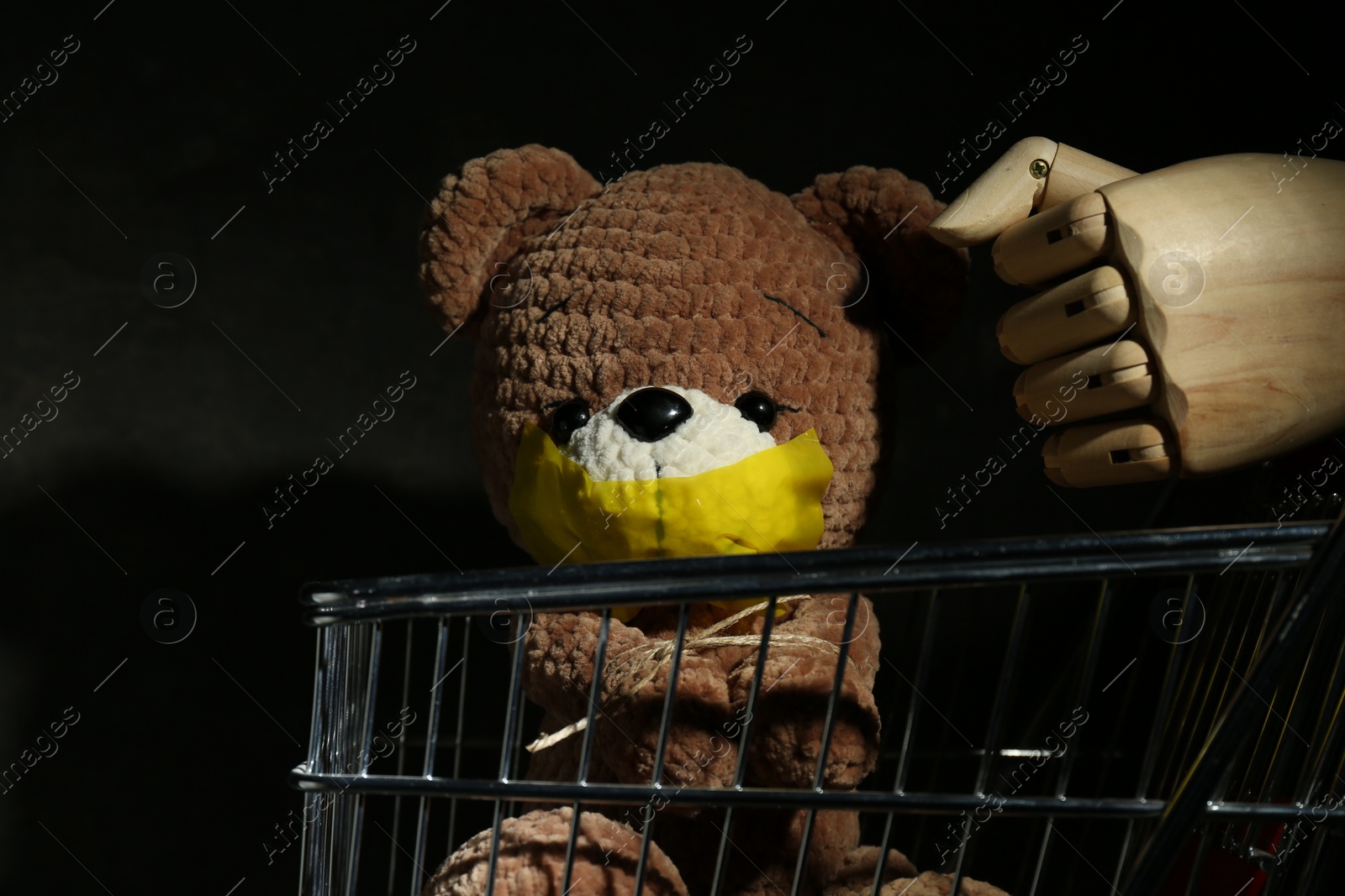 Photo of Stop child abuse. Mannequin hand and bear with taped mouth on black background, closeup