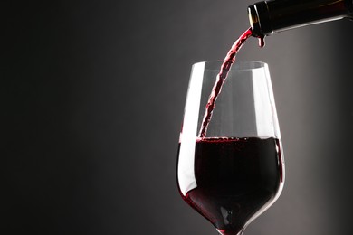 Photo of Pouring red wine into glass against grey background, closeup. Space for text