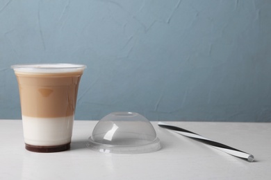 Plastic cup of tasty caramel macchiato on table, space for text