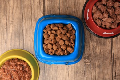 Dry and wet pet food in feeding bowls on wooden background, flat lay