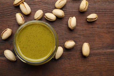 Photo of Delicious pistachio butter and ingredients on wooden table, flat lay