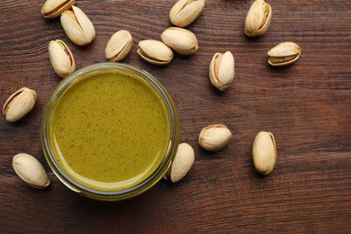 Delicious pistachio butter and ingredients on wooden table, flat lay