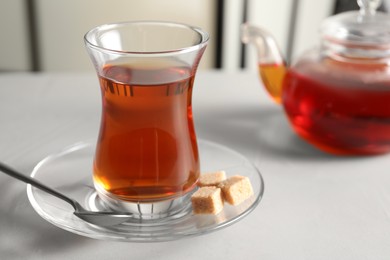 Traditional Turkish tea in glass and sugar cubes on white table, closeup. Space for text