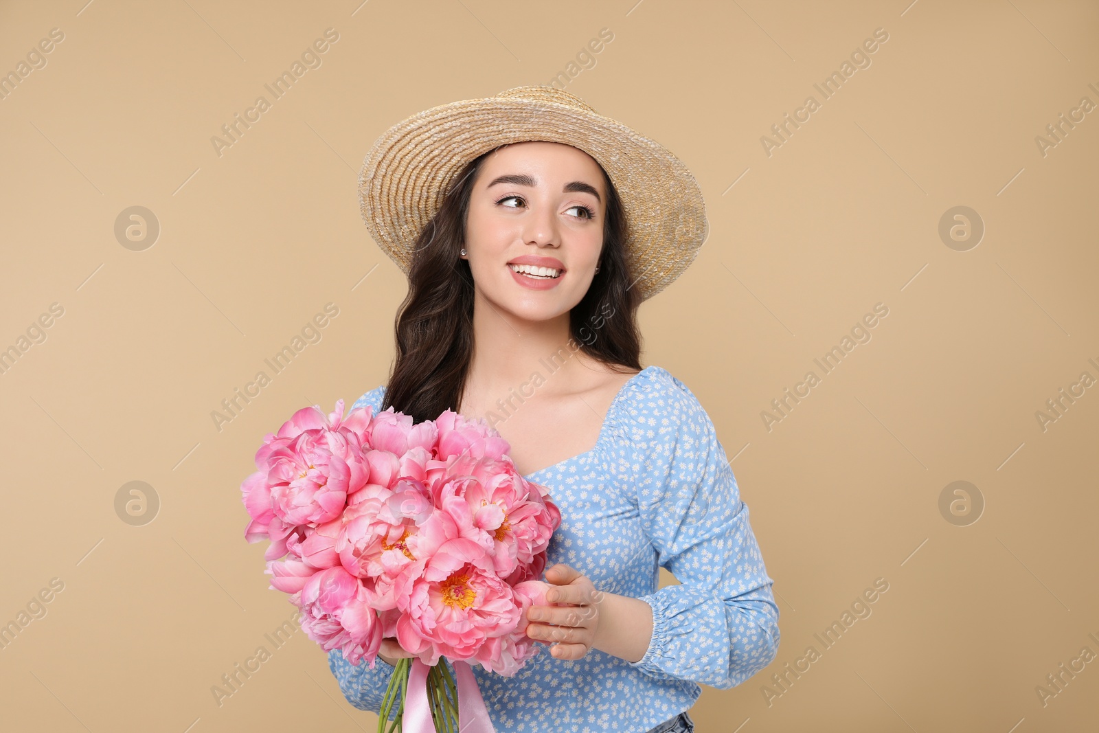 Photo of Beautiful young woman in straw hat with bouquet of pink peonies against beige background