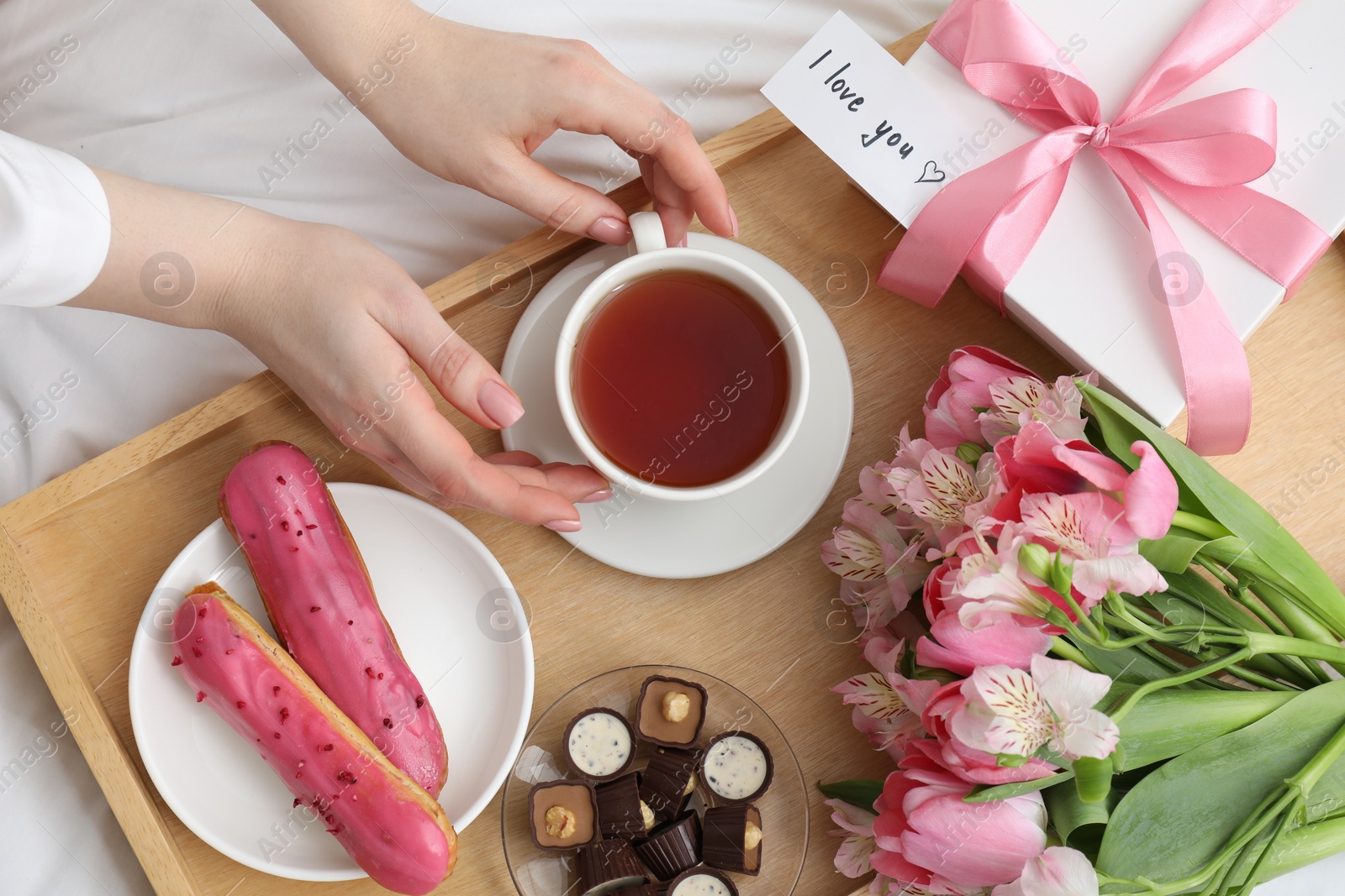 Photo of Tasty breakfast served in bed. Woman with tea, desserts, gift box, flowers and I Love You card at home, top view