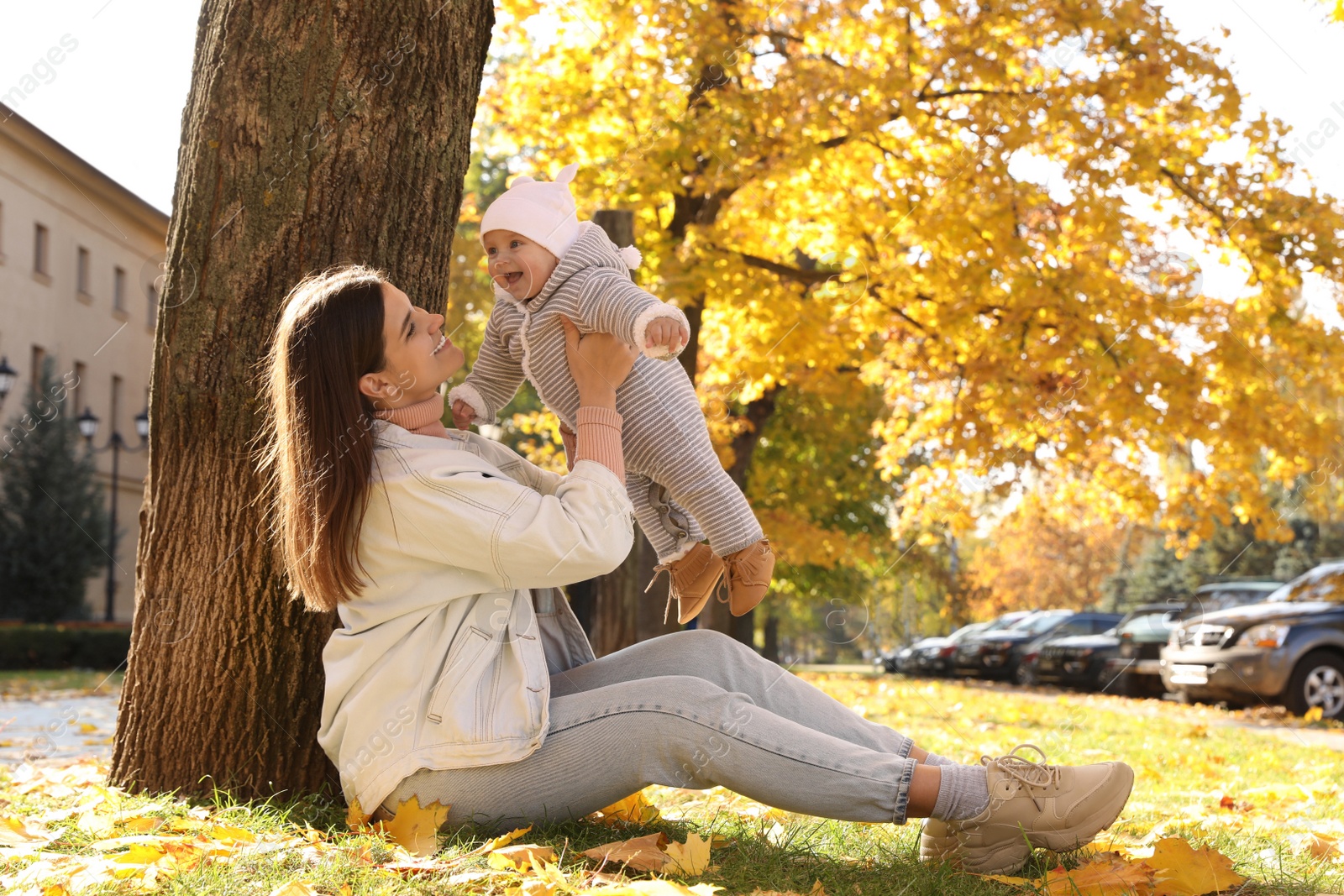 Photo of Happy mother with her baby daughter sitting near tree in park on sunny autumn day, space for text