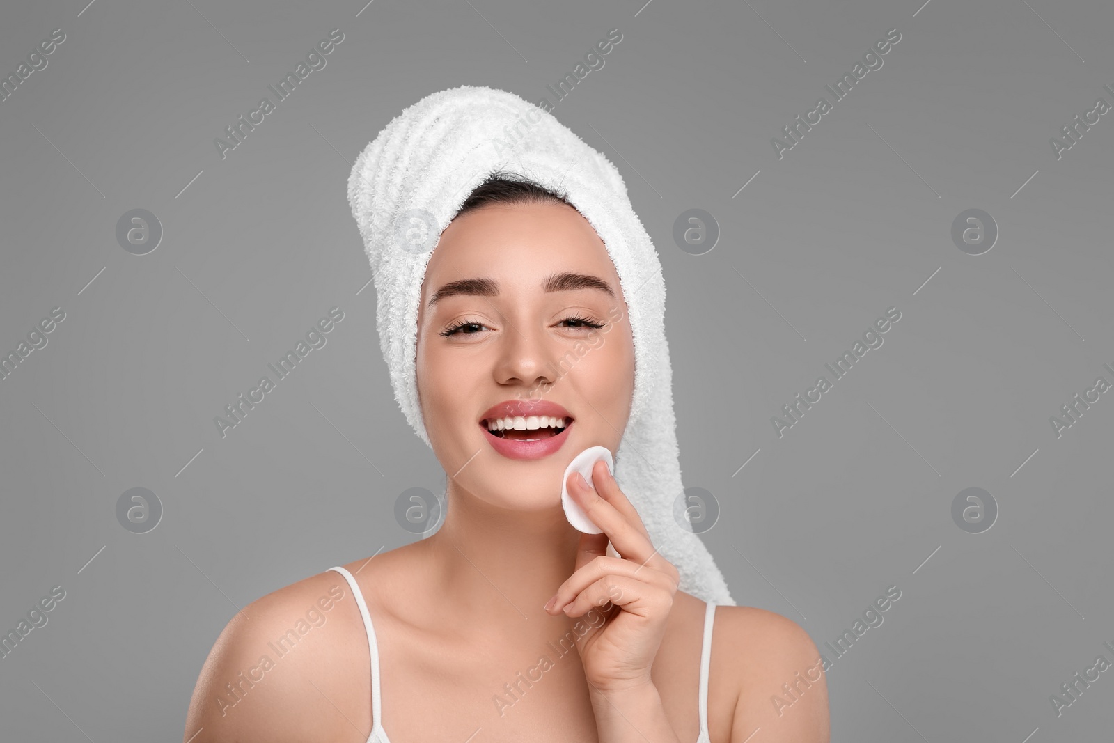 Photo of Beautiful woman in terry towel removing makeup with cotton pad on gray background