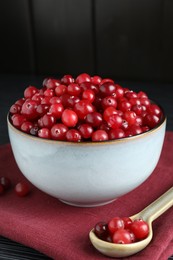 Photo of Cranberries in bowl and spoon on black wooden table, closeup