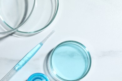 Pipette and petri dishes with liquid on white marble table, flat lay