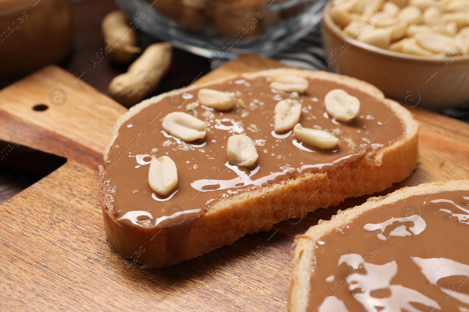 Photo of Toasts with tasty nut butter and peanuts on wooden board, closeup