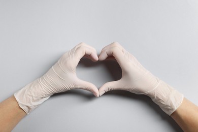 Photo of Doctor wearing white medical gloves making heart gesture on grey background, top view