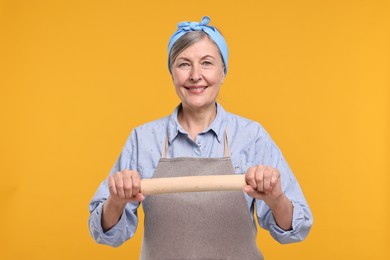 Happy housewife with rolling pin on orange background