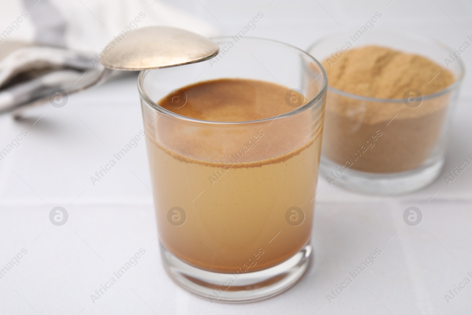 Photo of Soluble fiber with water in glass and powder on white tiled table, closeup