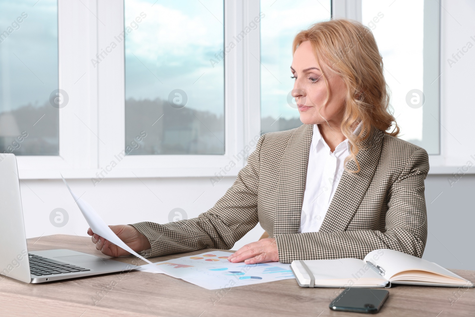 Photo of Lady boss with papers working near laptop at desk in office. Successful businesswoman