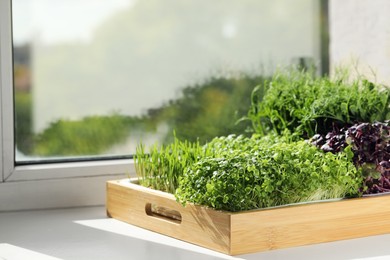Different fresh microgreens in wooden crate on windowsill indoors, space for text