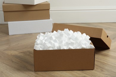 Photo of Cardboard box with styrofoam cubes on wooden floor indoors