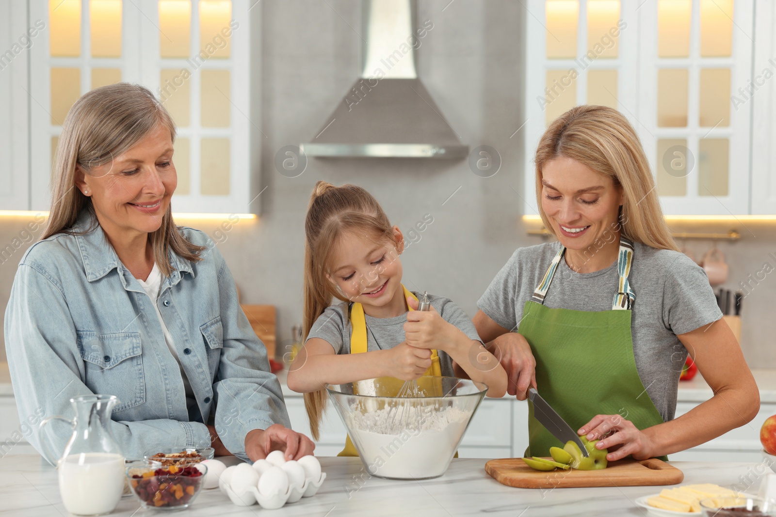 Photo of Three generations. Happy grandmother, her daughter and granddaughter cooking together in kitchen