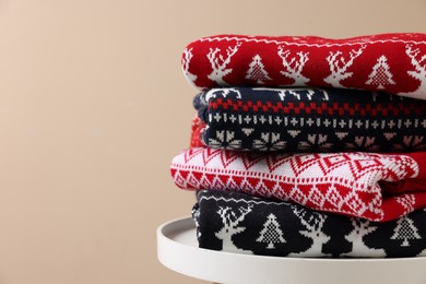 Photo of Stack of different Christmas sweaters on white table against beige background, closeup. Space for text