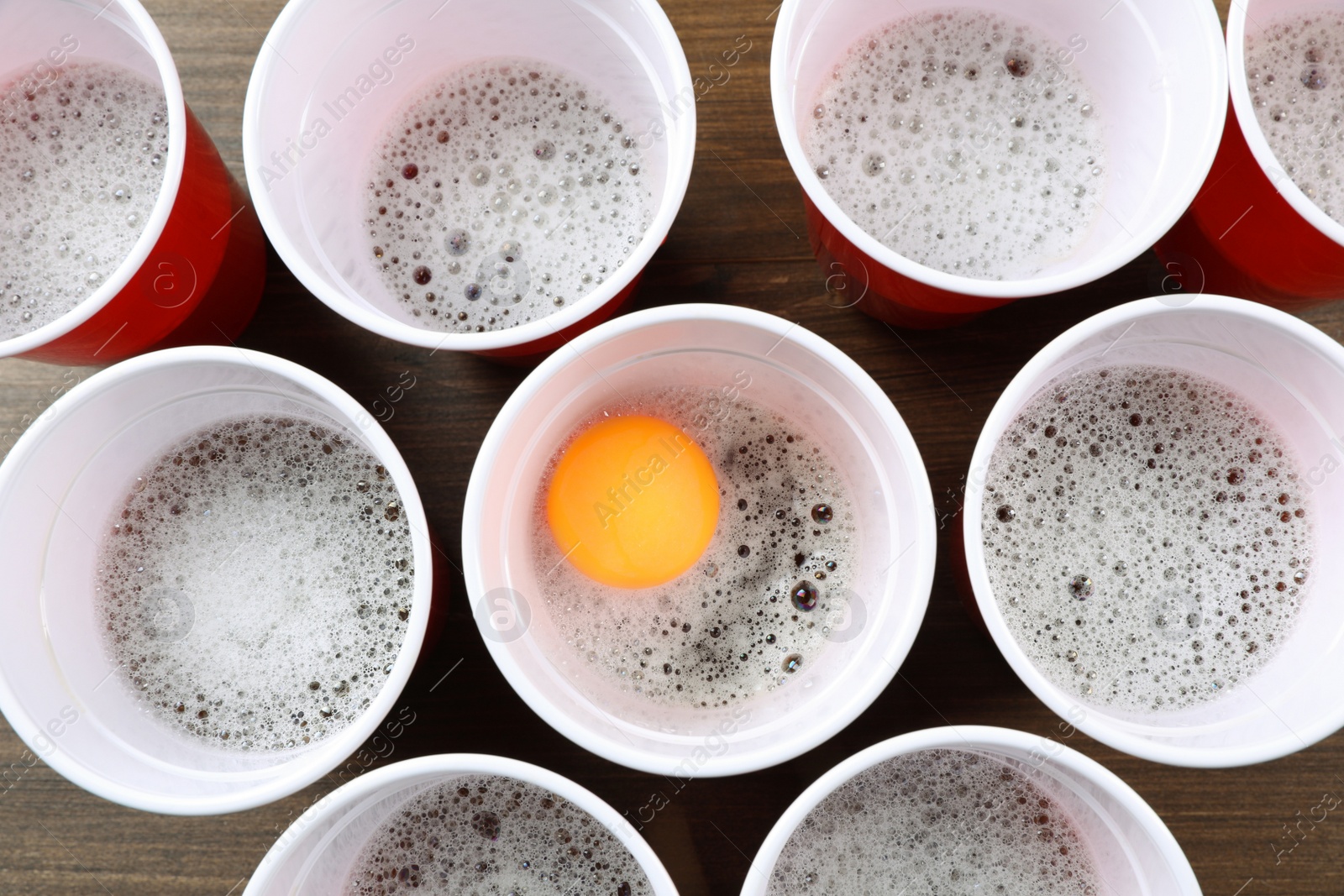 Photo of Plastic cups and ball for beer pong on wooden table, flat lay