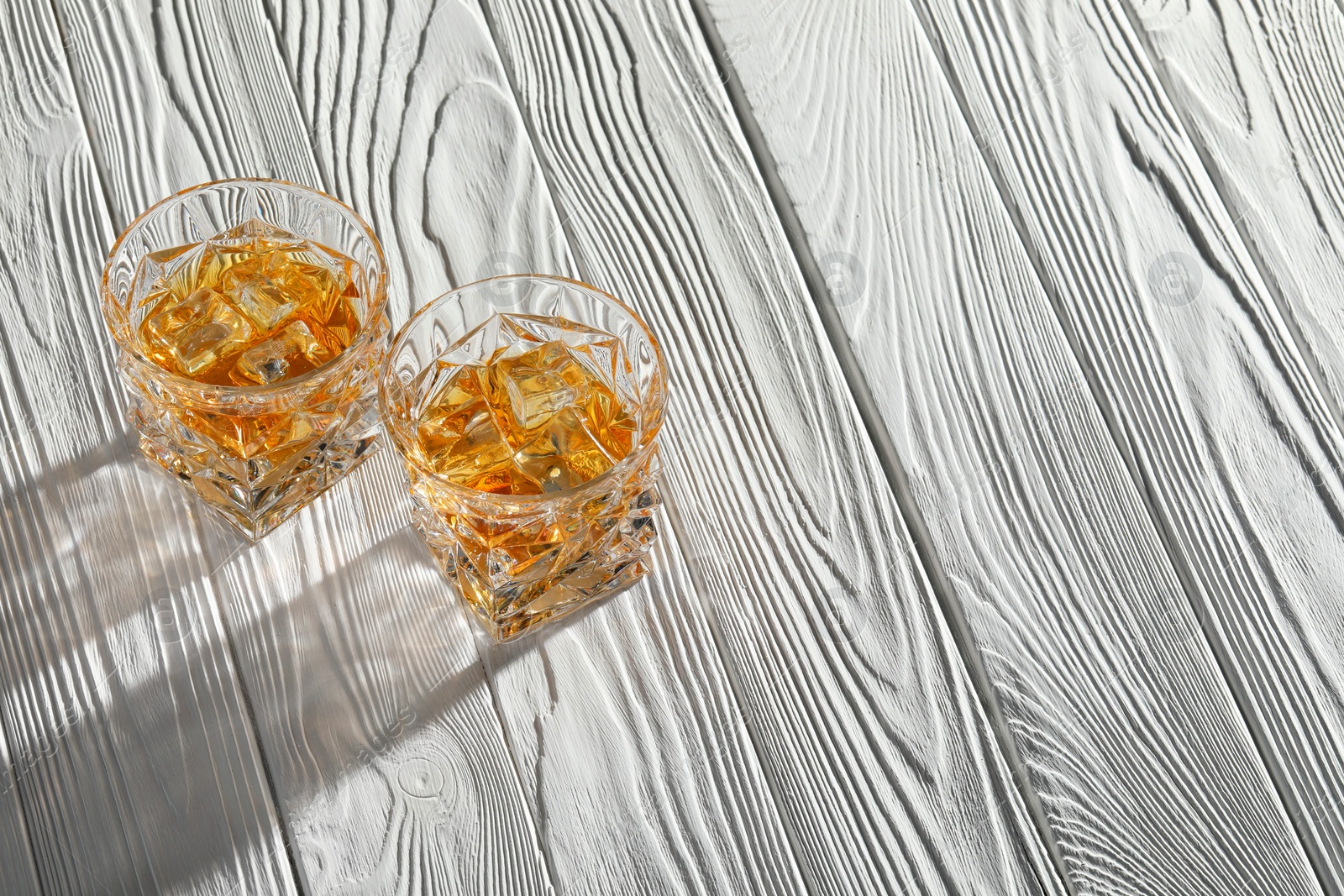 Photo of Whiskey with ice cubes in glasses on white wooden table, above view. Space for text