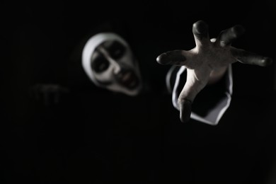 Photo of Scary devilish nun frightening against black background, focus on hand. Halloween party look