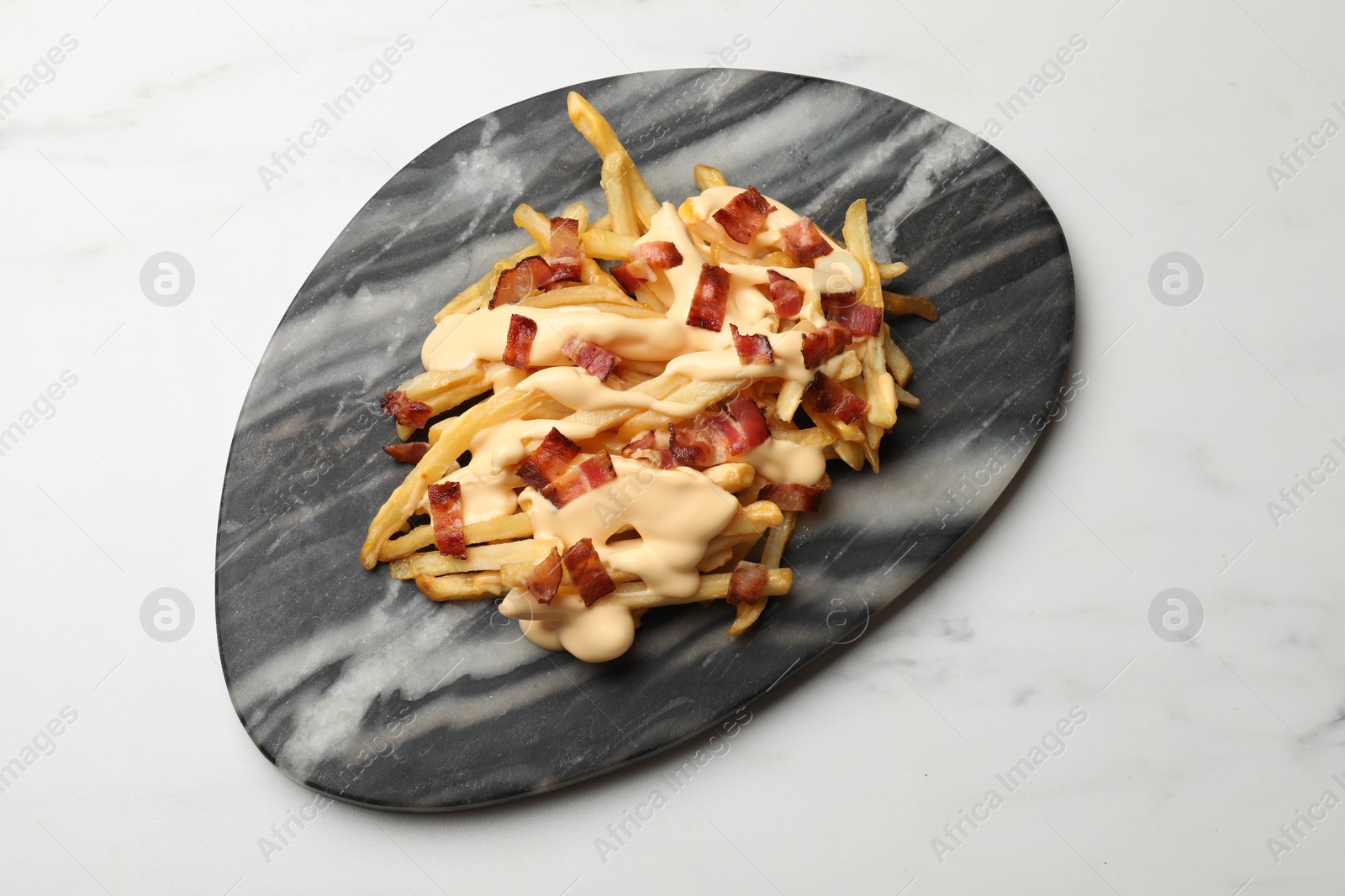 Photo of Delicious French fries with bacon and cheese sauce on white marble table, top view