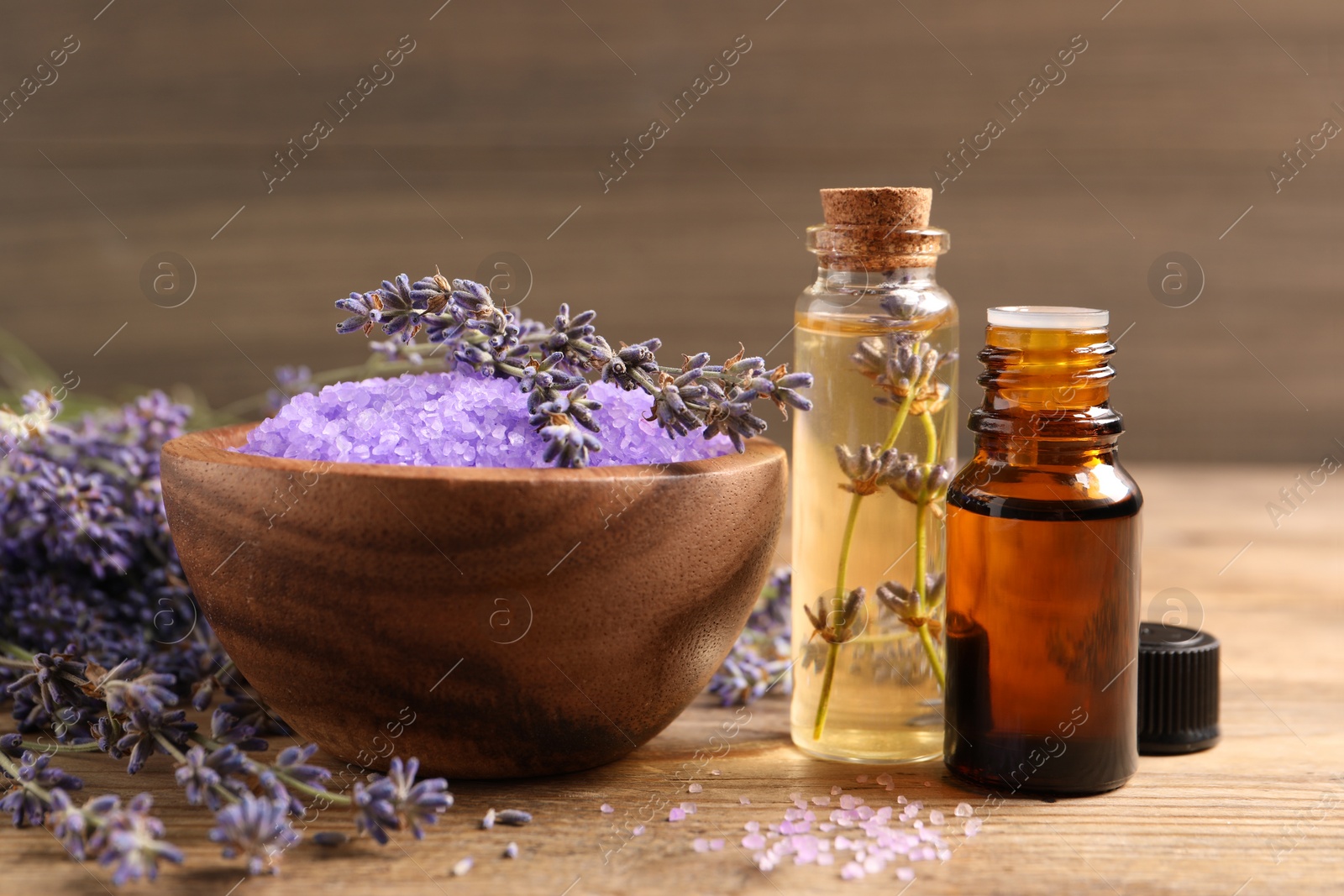 Photo of Bowl of sea salt, essential oil and lavender flowers on wooden table