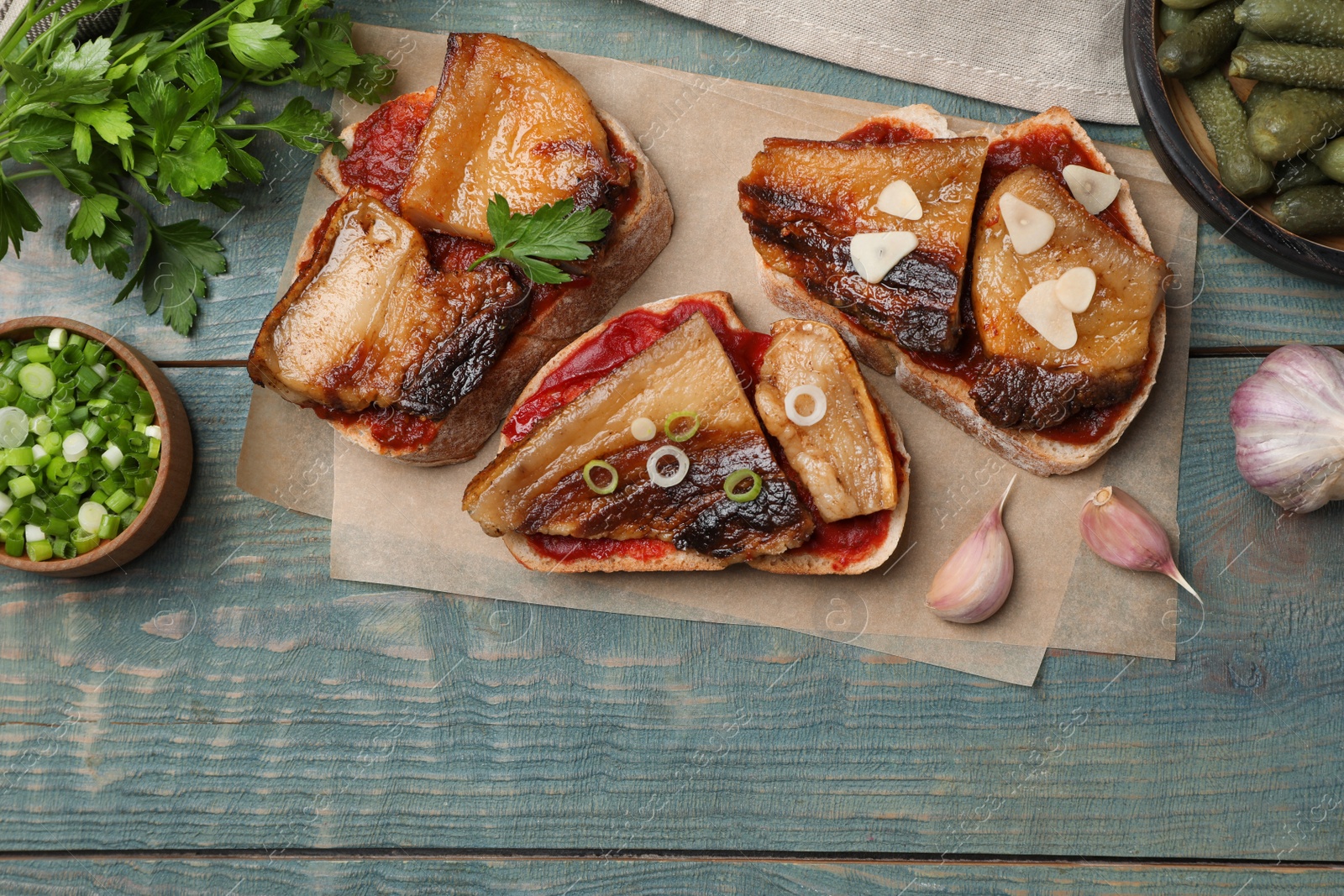 Photo of Tasty sandwiches with fried pork fatback slices on light blue wooden table, flat lay