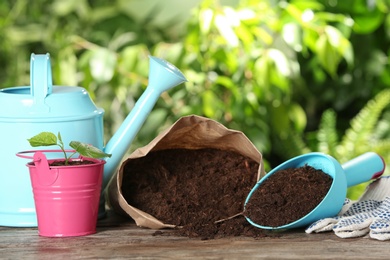 Composition with bag of soil and gardening equipment on wooden table against blurred background, space for text