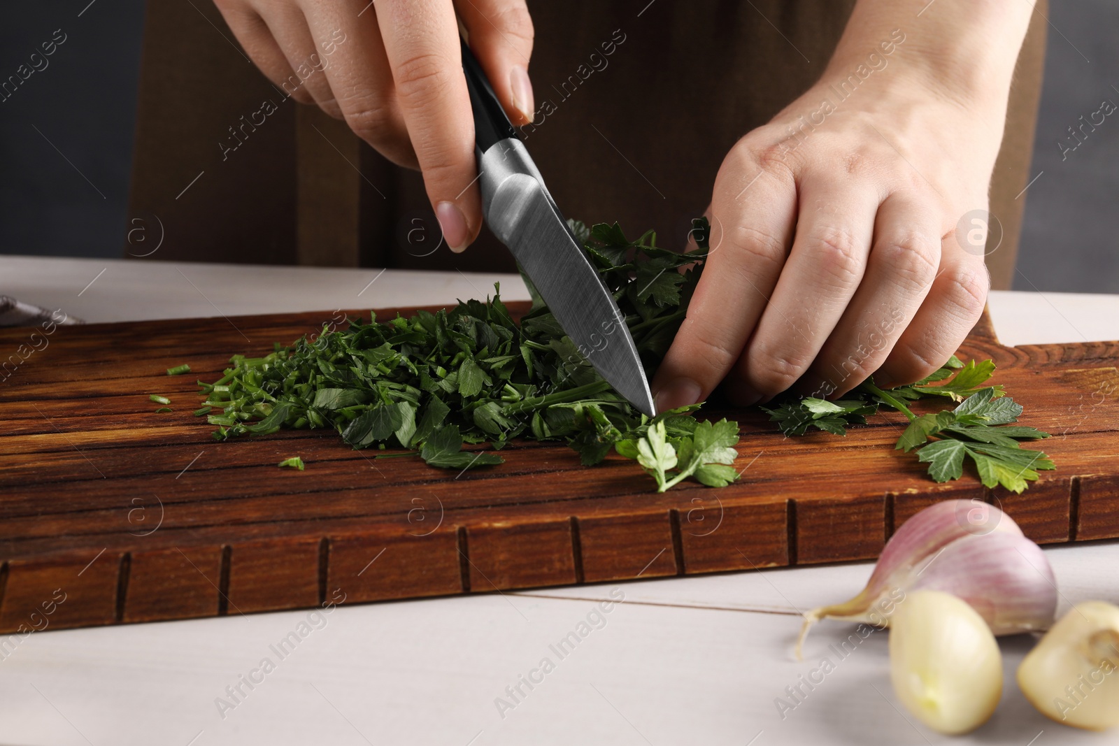 Photo of Woman cutting fresh parsley at white wooden table, closeup