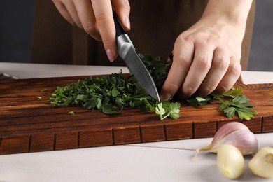 Woman cutting fresh parsley at white wooden table, closeup